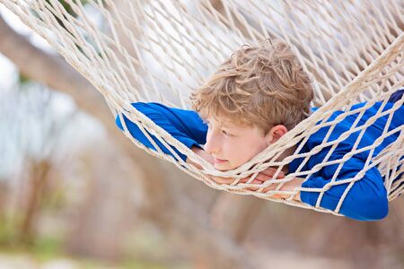 smiling boy in blue swimwear relaxing in hammock at the beach enjoying tropical vacationの写真素材