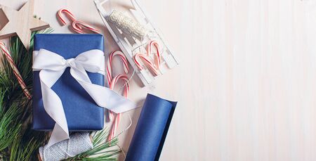cold toned panorama of flatlay image of nicely wrapped christmas gift with wrapping paper, ribbons, tree branches and candy canes, copy space on rightの写真素材