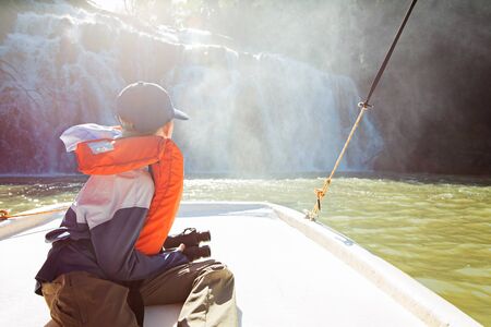 little boy with binoculars enjoying the view of waterfalls from the boat traveling at parana river,...