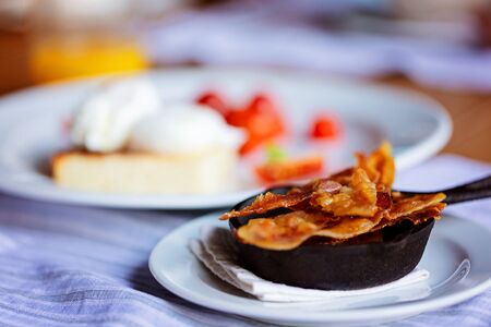 close-up of sliced bacon served in small pan with eggs and tomatoes in the background, gourmet hotel breakfastの写真素材