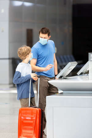 family of two, father and son, in face masks standing with the luggage in the airport, travel during coronavirus pandemic conceptの写真素材