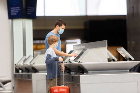 family of two, father and son, in face masks standing with the luggage in the airport, travel during coronavirus pandemic conceptの写真素材