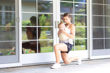 busy young mother doing fitness at home together with her baby during stay-at-home order, healthy family activity conceptの写真素材