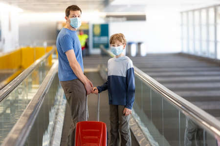 family of two, father and son, in face masks standing with the luggage in the airport, travel during coronavirus pandemic conceptの写真素材