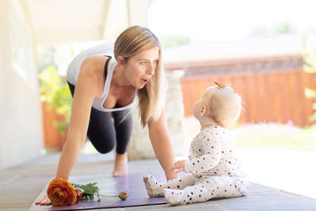 busy young mother doing yoga fitness at home together with her baby during stay-at-home order, healthy family activity conceptの写真素材