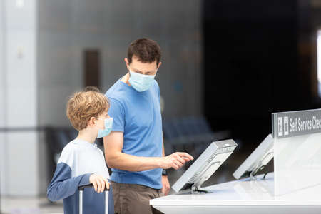 family of two, father and son, in face masks standing with the luggage in the airport, travel during...