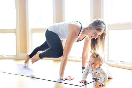 busy young mother doing yoga fitness at home together with her baby during stay-at-home order, healthy family activity conceptの写真素材