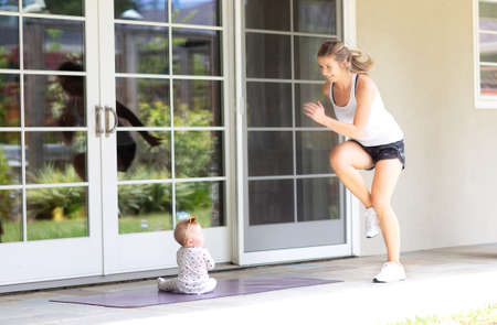busy young mother doing cardio fitness at home together with her baby, healthy family activity conceptの写真素材