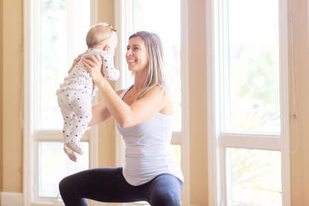 busy young mother doing fitness at home together with her baby during stay-at-home order, healthy family activity conceptの写真素材