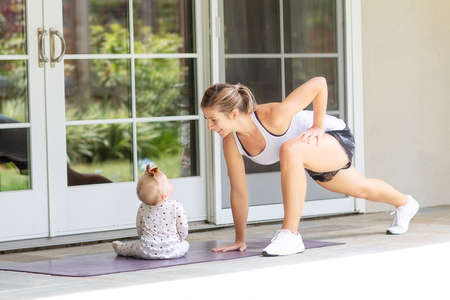 busy young mother doing streching fitness at home together with her baby, healthy family activity conceptの写真素材