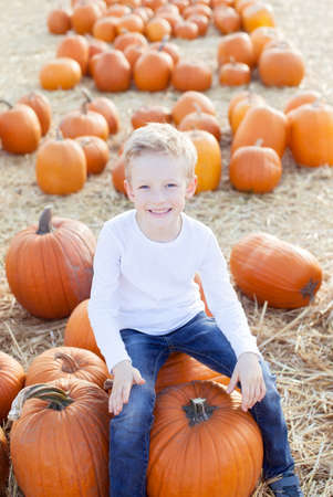 smiling little boy sitting on a pumpkin at pumpkin patch, fall season conceptの写真素材
