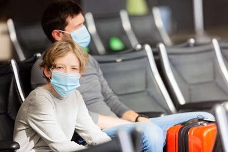 family of two, father and son, wearing face masks sitting in airport terminal, travel during coronavirus pandemic conceptの写真素材
