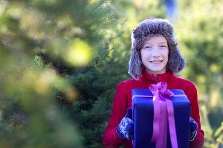 smiling cheerful boy holding nicely wrapped christmas present and enjoying outdoor christmas time, copy space on left, holiday conceptの写真素材