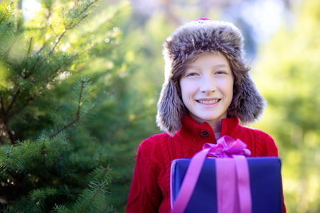 smiling cheerful boy holding nicely wrapped christmas present and enjoying outdoor christmas time,...