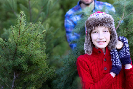 cheerful smiling boy and his dad carrying freshly cut tree at outdoor christmas tree farm, fun holiday family activity, copy space on leftの写真素材