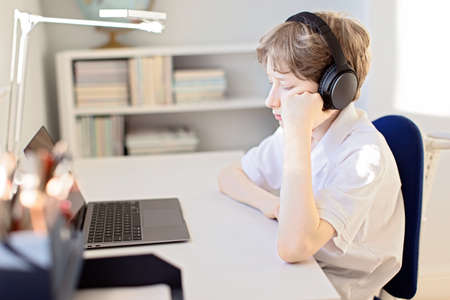 upset tired boy online learning at home during  pandemic using laptop and headphonesの写真素材