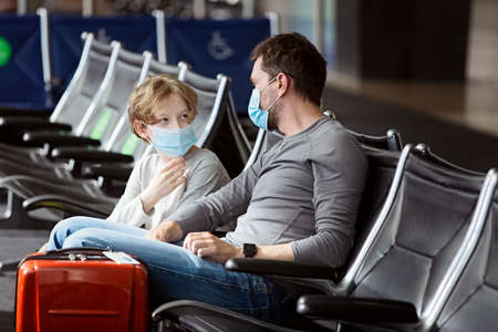 family of two, father and son, wearing face masks sitting in airport terminalの写真素材