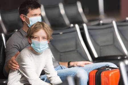 family of two, father and son, wearing face masks sitting in airport terminalの写真素材