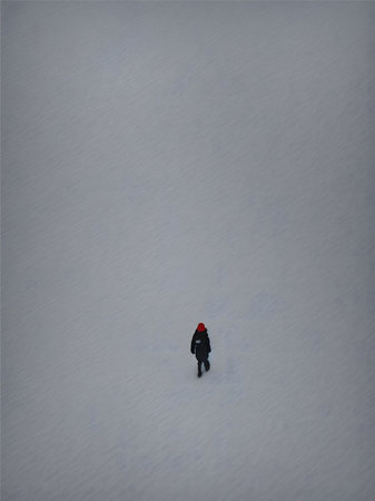 A lone figure walks through a pristine field of snowの素材
