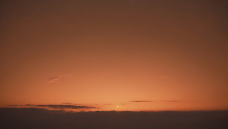 Soft, glowing sunset or sunrise sky, fading from a dark orange at the horizon to a lighter orange at the top, with a thin layer of clouds just above the horizonの素材