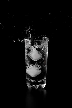 Ice cubes thrown to a glass of water from above with splash on a black backgroundの写真素材