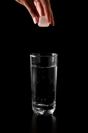 Ice cubes thrown to a glass of water from above with splash on a black backgroundの写真素材