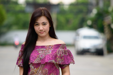 Portrait of lady attractive and smiling caucasian lady standing with Wearing a purple dress on background of tree blurry.の写真素材