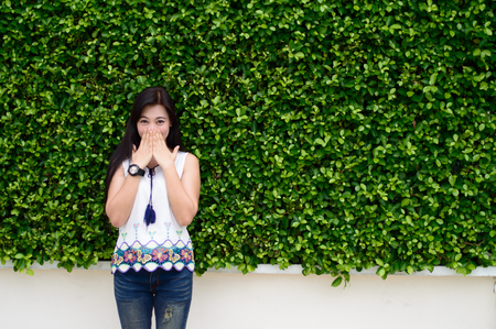 Portrait of lady standing and Hands gag action with Wearing a white shirt with jeans And wearing a watch on The background is green leafの写真素材