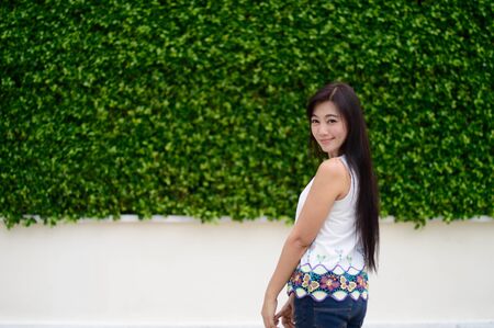 Portrait of lady standing and Stand back and turned back action with Wearing a white shirt with jeans on The background is green leafの写真素材
