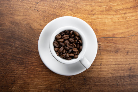 Coffee beans in a white cup on a wooden background.