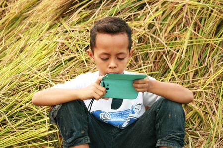 boy play in the paddy filed with his mobile phone