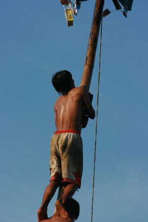 Male Indonesian bamboo pole climbing wet slippery for prizes in a ceremony commemorating the Indonesian Independence Day every August 17のeditorial素材
