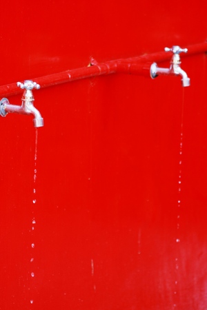 Water flows from an old tap on a red backgroundの写真素材