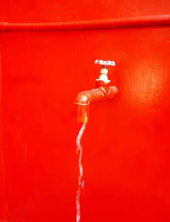 Water flows from a tap on a red backgroundの写真素材