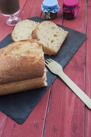 a vertical view of a homemade sponge cake with a coffee and two little jam jars