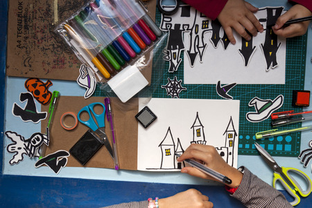 a horizontal overhead view of two little children's hands creating some Halloween decorations