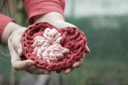 a horizontal frontal view of a crochet heart being offered by a woman hands with space for a messageの写真素材