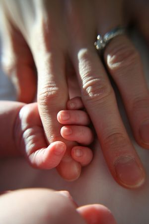 Baby grasping mother's finger in sunlight