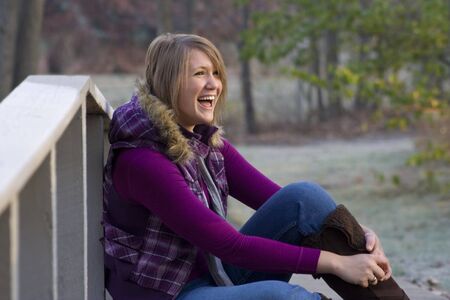 A teenage girl in a winter coat laughs in a park settingの写真素材