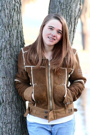 A teenage girl in a winter coat leans against a tree and smilesの写真素材