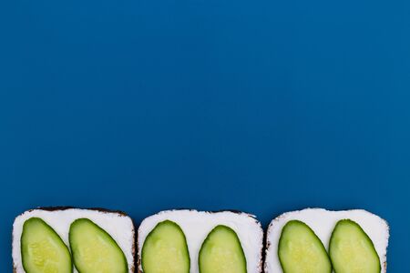 Sandwiches with soft cheese and cucumber - delicious healthy breakfast, snack. Flat lay with copy space on blue background.の写真素材