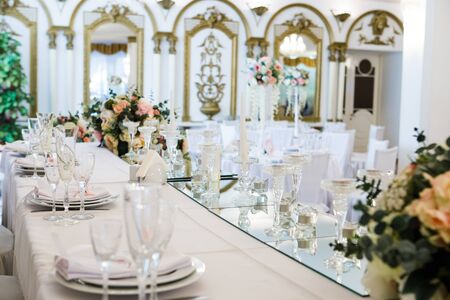 Table served for newlyweds dinner in luxury restaurant. White candles, cutlery on mirror, decorations with flowers. Decorated hall, nobody.の写真素材