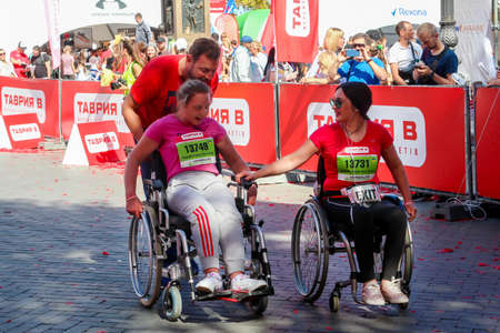 ODESSA, UKRAINE - CIRCA SEPTEMBER, 2019: Two women wheelchair competitors support each other at half-marathon in Odessa. Concept of disabled and sports.のeditorial素材