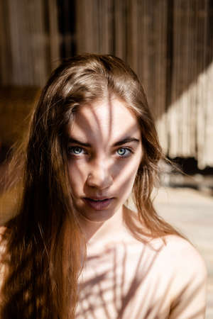 Fashion portrait of young blondish woman with shadows on her face. Light and shadow. interesting portrait of young girl's face covered with unusual shadow.の写真素材