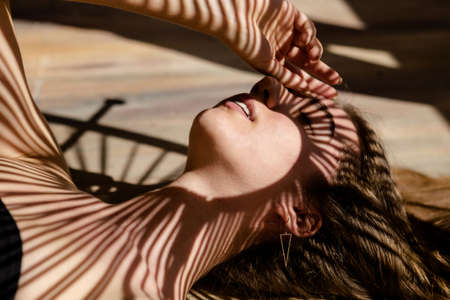 Portrait of beautiful female model with shadows of palm leaf on her face. Concept of sunbathing, vacation, relaxation.の写真素材