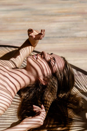 Portrait of young woman with shadows of palm leaf on her face. Concept of sunbathing, vacation, summer time.の写真素材