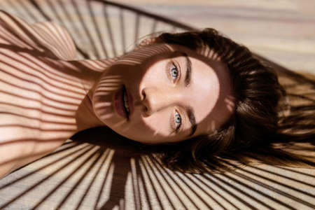 Portrait of beautiful woman with shadows of palm leaf on her face. Concept of sunbathing, vacation.の写真素材