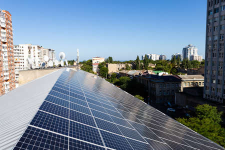 Solar panels on roof, view on city with buildings and trees. Concept of renewable energy technologies, saving environment.の写真素材