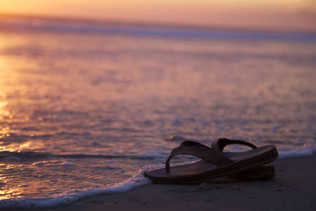Sandals Near Water on a Beach Sunsetの写真素材