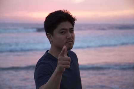 Young Asian Man Finger Gun Pointing at Ocean Sunsetの写真素材